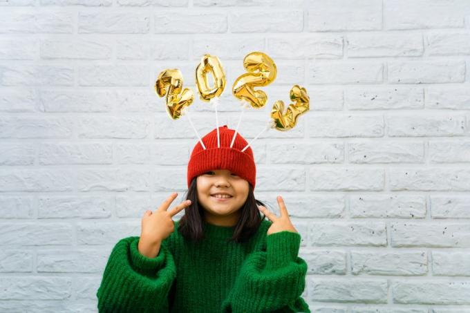 vesela azijska punčka v zelenem puloverju od blizu z zlatimi baloni s številkami 2023 v prostoru za kopiranje klobuka, ozadje bele opečne stene, dekle, ki gleda v kamero, se smeji