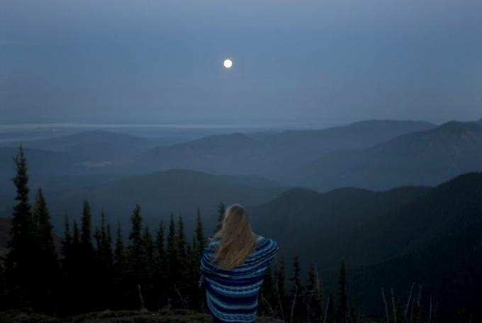 ženska, zavita v odejo, gleda gorsko pokrajino s polno luno, pogled od zadaj