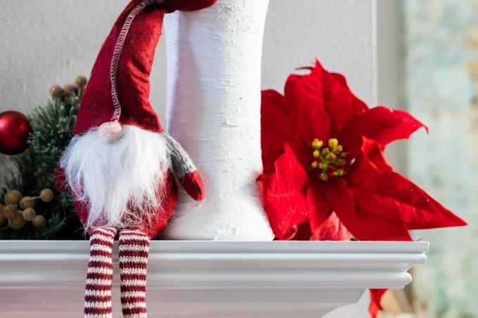 klasičen norveški praznični božični okras v obliki palčka, ki sedi na belem modernem plašču z belo vazo z evkaliptusom in cvetom božične zvezde