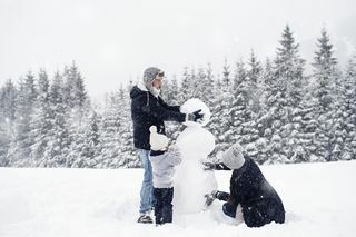 tričlanska družina v snegu gradi snežaka