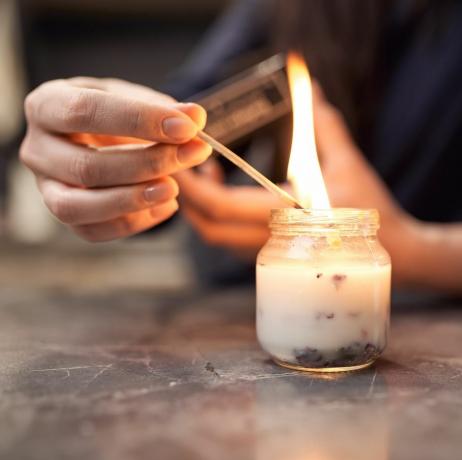 obrezovanje anonimna ženska z gorečo vžigalico, aromatična sveča v steklenem kozarcu, postavljena na marmorno mizo doma