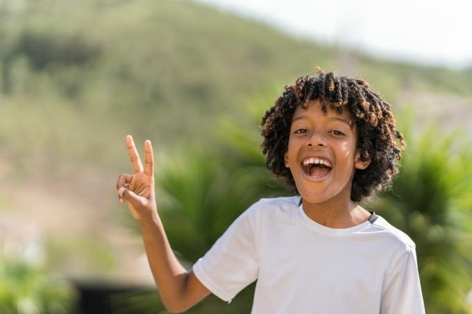 10-letni afroameriški deček se glasno smeji, medtem ko postavlja znak miru