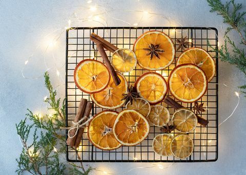 posušene pomaranče, limone, cimetove palčke in janeževe zvezde na ozadju božičnih lučk in jelkovih vej sestavine za kuhanje ali božično dekoracijo ravno položen prostor za besedilo