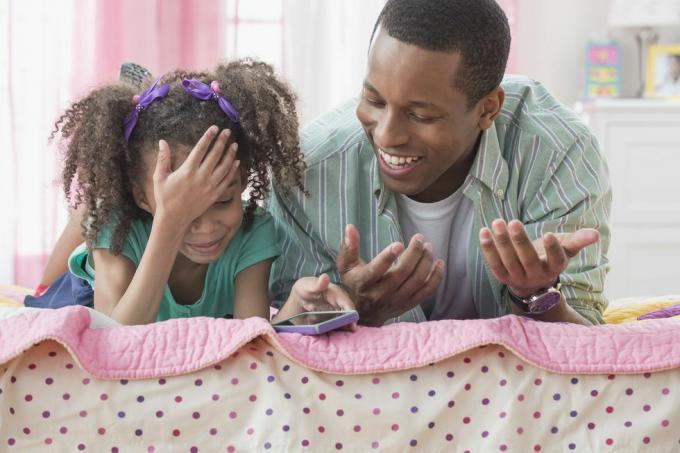 oče in hči uporabljata mobilni telefon skupaj na postelji