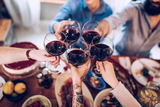 dlani in roke petih ljudi, ki nazdravljajo s kozarci rdečega vina za večerjo