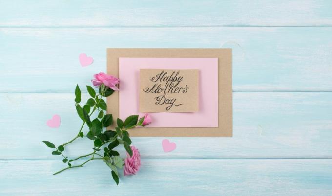 ročno izdelana čestitka s sporočilom materinski dan na pobarvani bledo modri mizi z rožnatimi vrtnicami