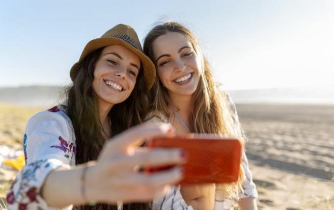 dva najboljša prijatelja, ki na plaži posnameta selfi s pametnim telefonom