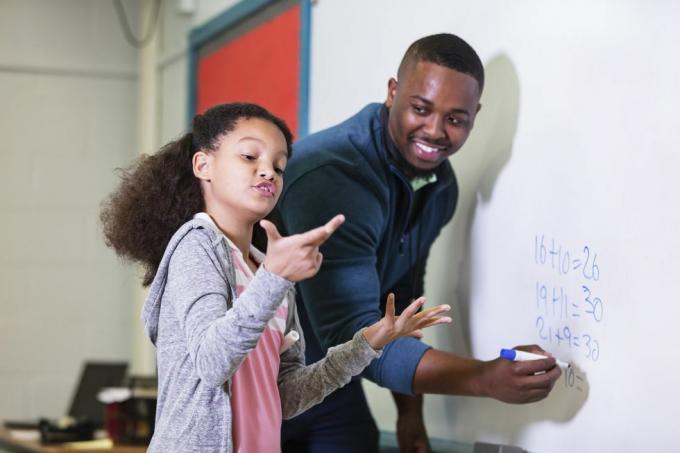 večrasna 9-letna deklica pri pouku matematike, ki stoji za tablo s svojim učiteljem, mladim Afroameričanom v 20. Učitelj gleda svojega osnovnošolca in čaka, medtem ko ona poskuša ugotoviti odgovor, poudarek je na dekle