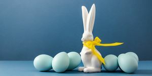 več modro barvanih velikonočnih jajc in bel velikonočni zajček z rumeno pentljo na mizi koncept prazničnega lova na jajca in barvanja