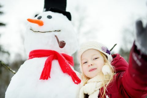 Očarljiva deklica, ki gradi snežaka v čudovitem zimskem parku. Simpatičen otrok, ki se igra v snegu.