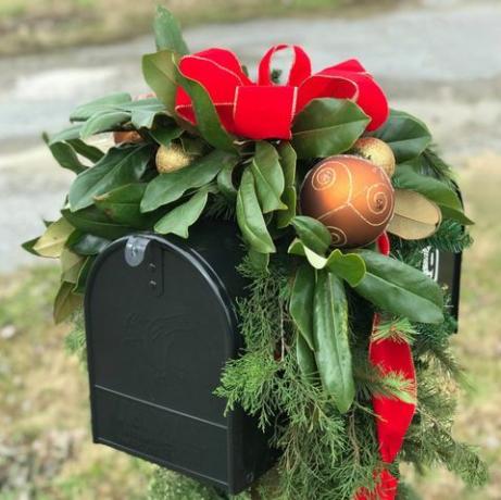 črni poštni predal, okrašen za praznike z zlatimi božičnimi kroglicami, rdečim trakom in veliko zelenja, vključno z listi magnolije in cedre