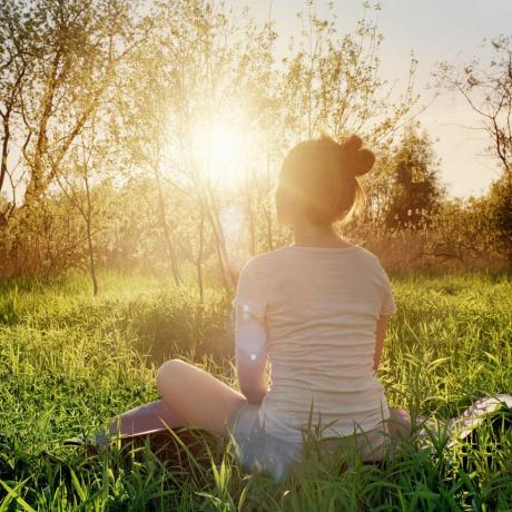 mlada ženska, ki sedi v položaju joge in uživa v sončnem zahodu v naravi