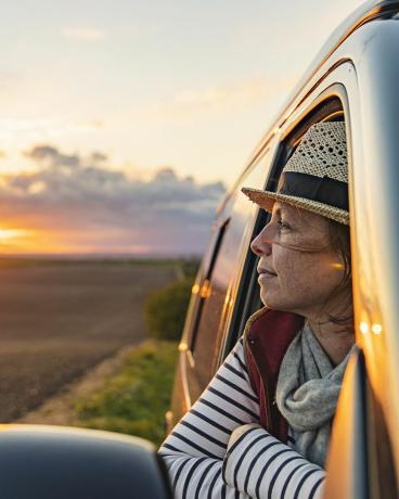 ženska v svojih 40-ih gleda na podeželje iz svojega avtodoma izgleda zadovoljno in sproščeno