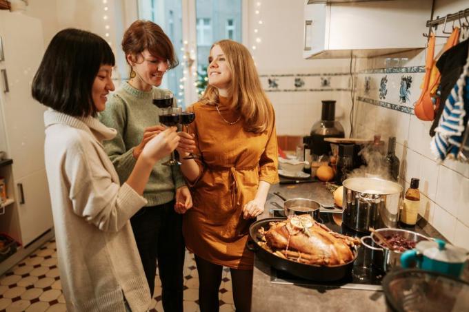 tri ženske, ki pijejo rdeče vino, medtem ko doma pripravljajo puranji obrok s puranom in tremi lonci na štedilniku, ki kuhajo